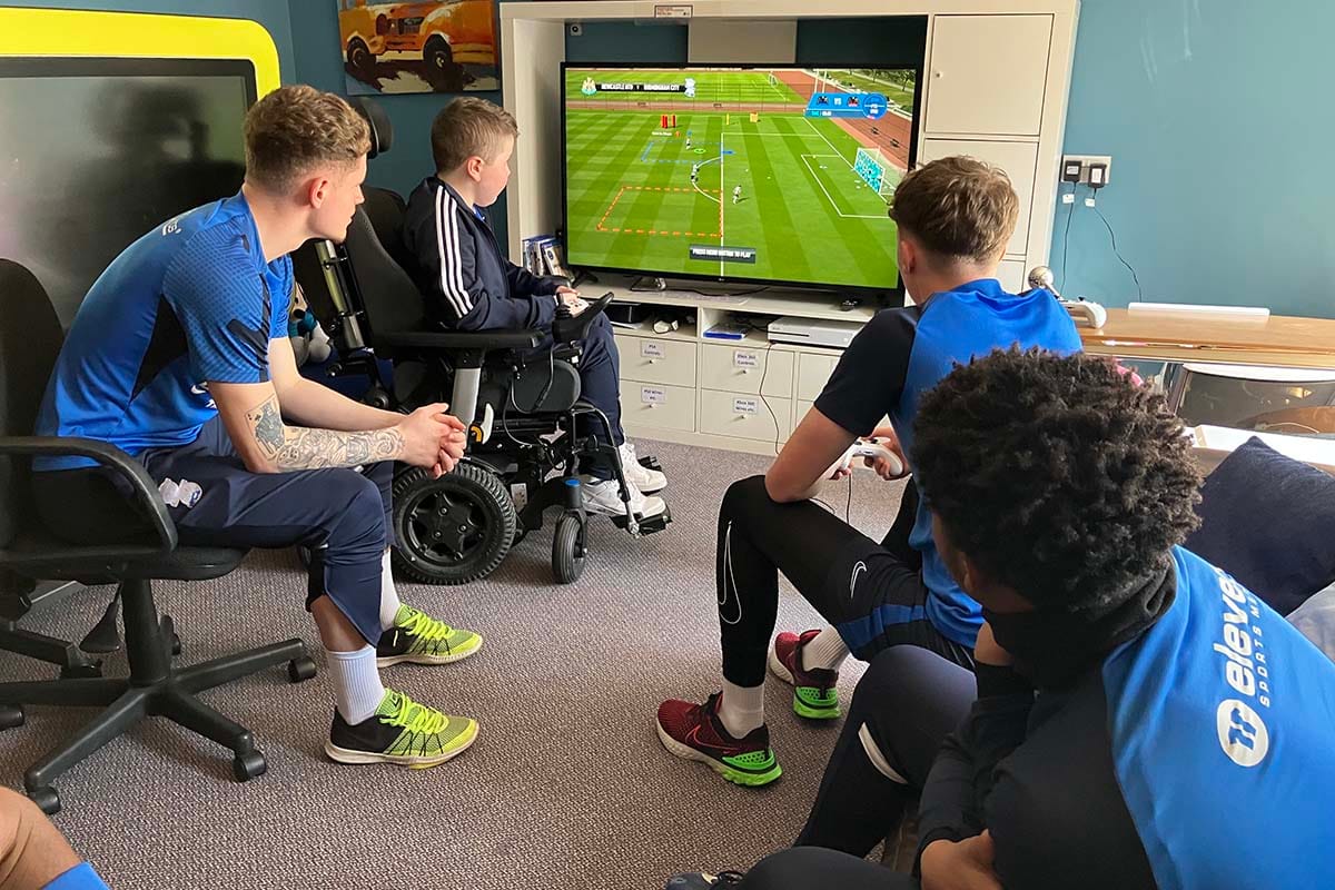 Group of boys gathered around TV screen watching boy in wheelchair play video game