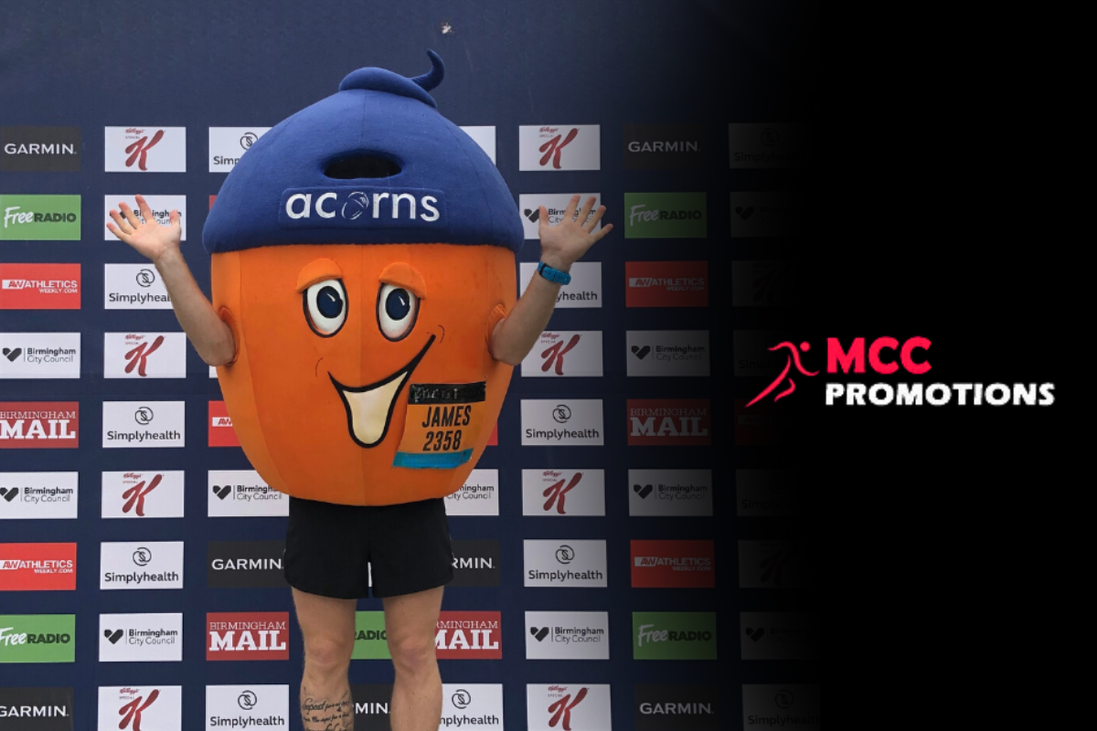 Alex the Acorns standing on stage with MCC Promotions logo to the right.