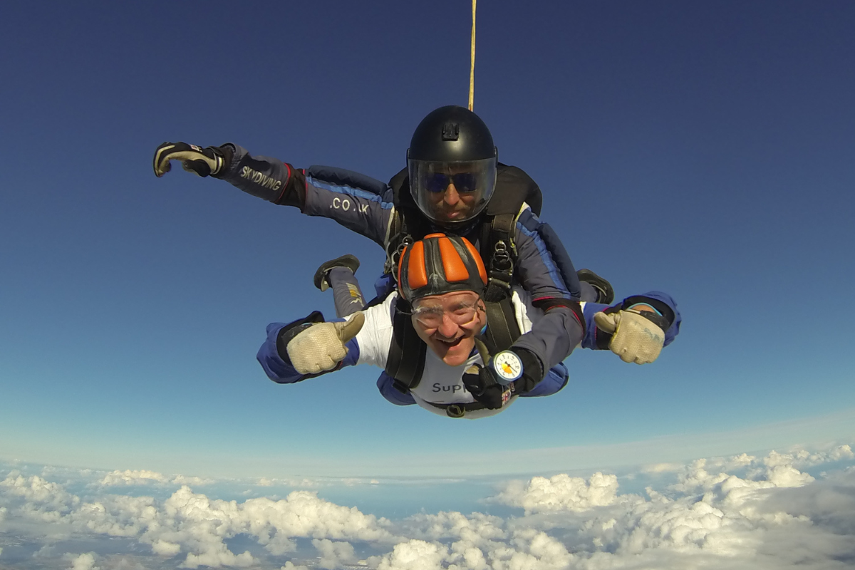 An Acorns supporter is tandem skydiving. He is smiling and giving a thumbs up