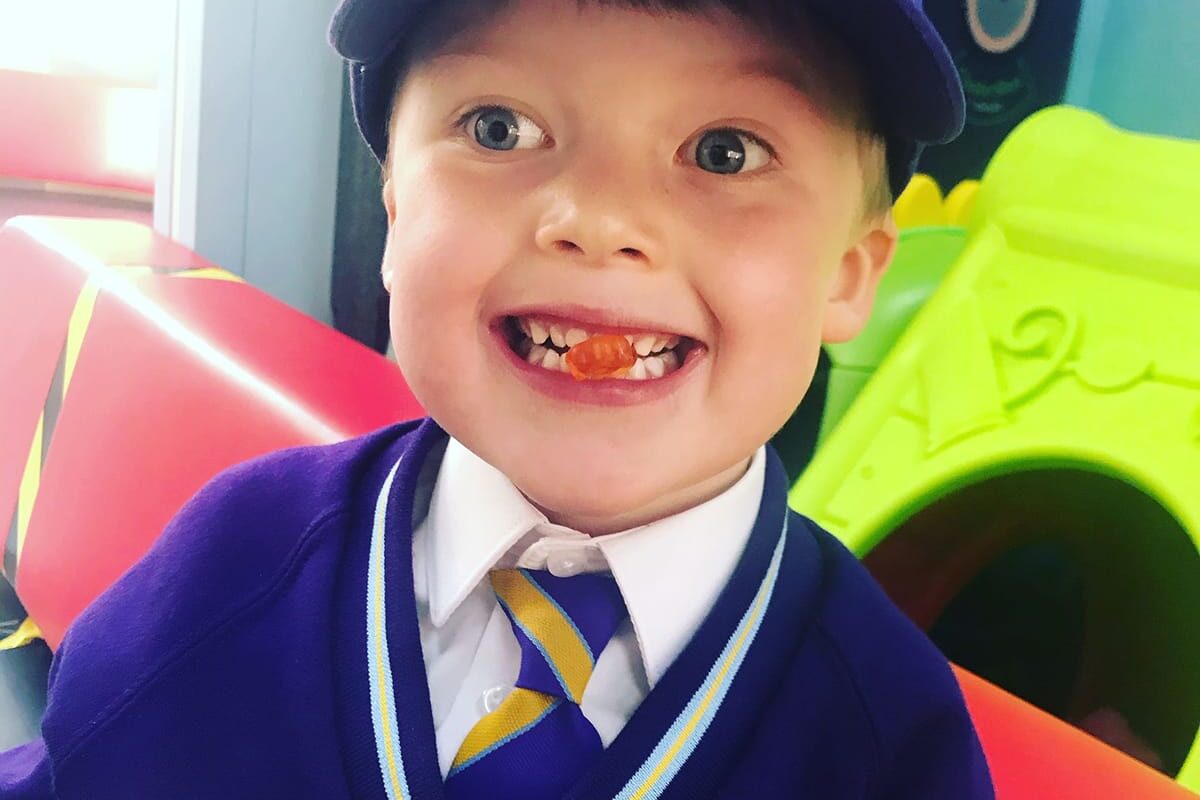A boy smiling at the camera with a gummy bear in between his teeth