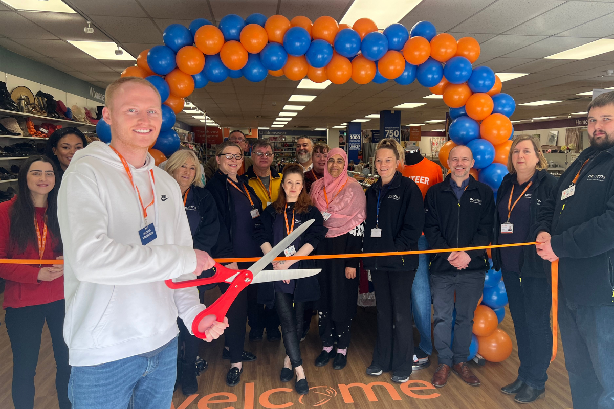 An Acorns shop volunteer cuts the ribbon declaring Acorns Erdington superstore open. He is using large scissors and stands in front of a balloon arch