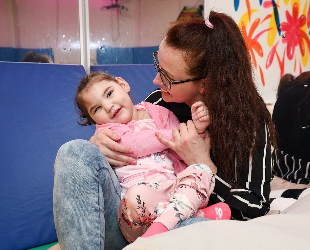A woman holds a little girl in her arms, who is smiling
