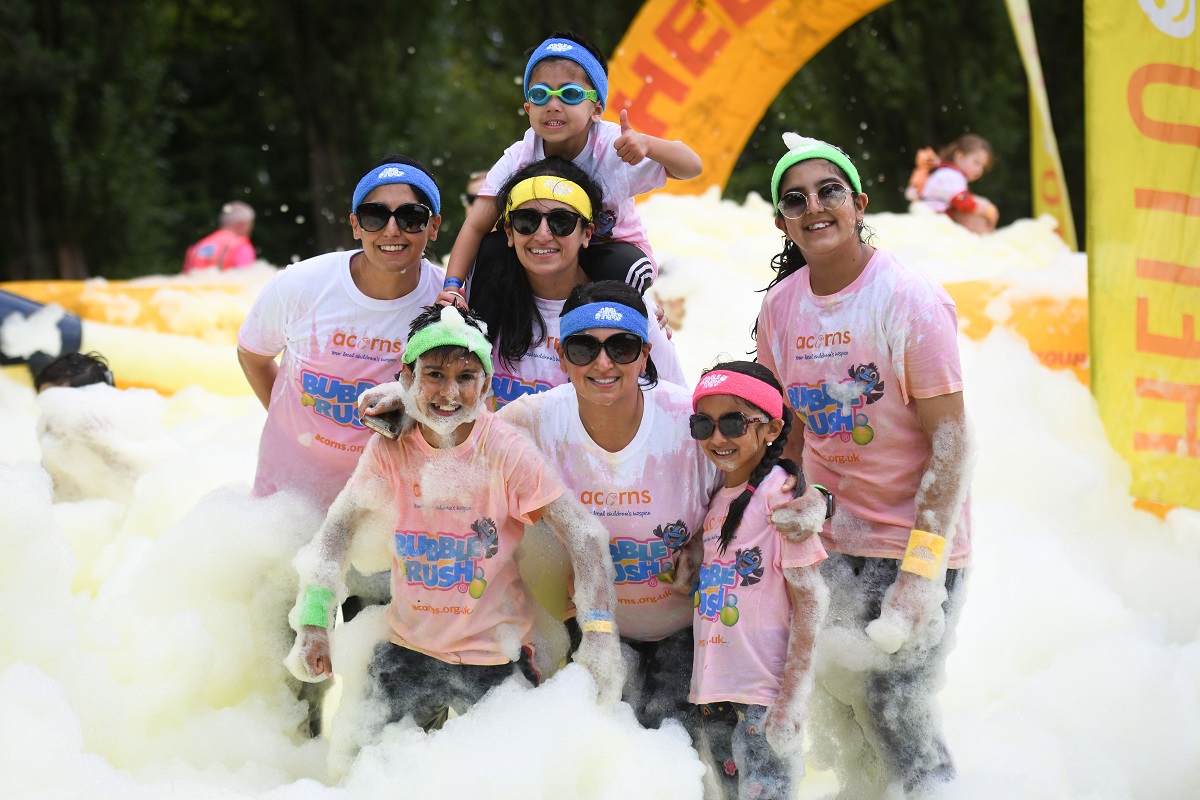 A family wearing sunglasses and colourful headbands pose in the yellow bubbles at Acorns Bubble Rush