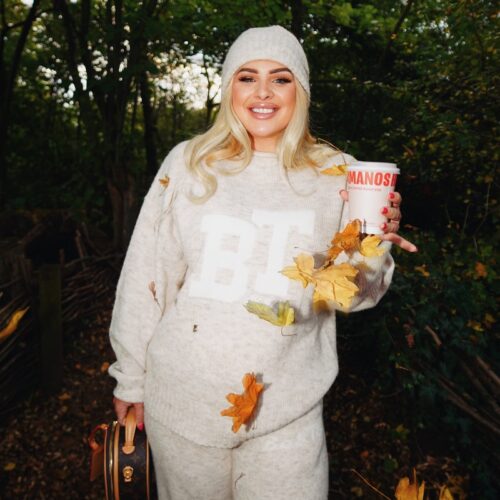 A woman stands outside, wearing a beanie hat and holding a takeaway coffee cup