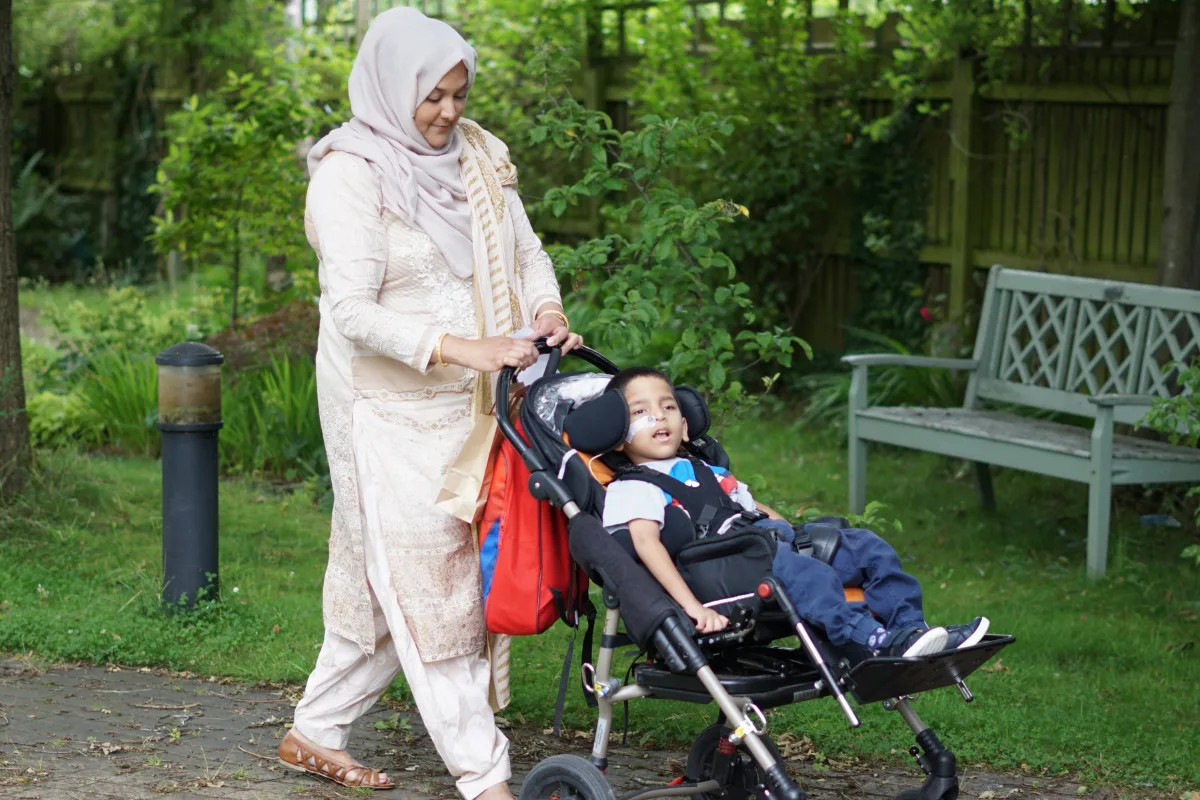 A mother pushing a young boy in a pushchair outside.