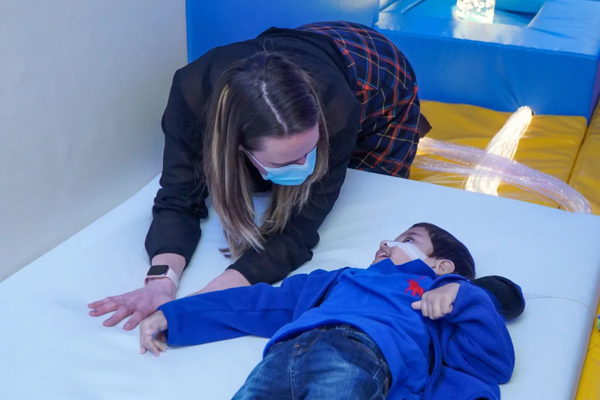 A young boy with a tube going into his nose lying down. A nurse is looking at him next to him.