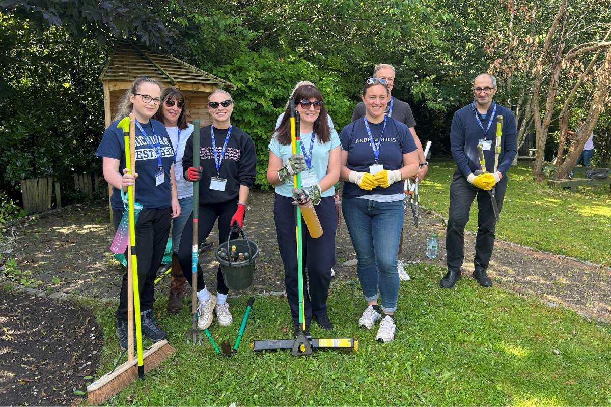 A small group of people stood outside, some of them are holding large brooms.