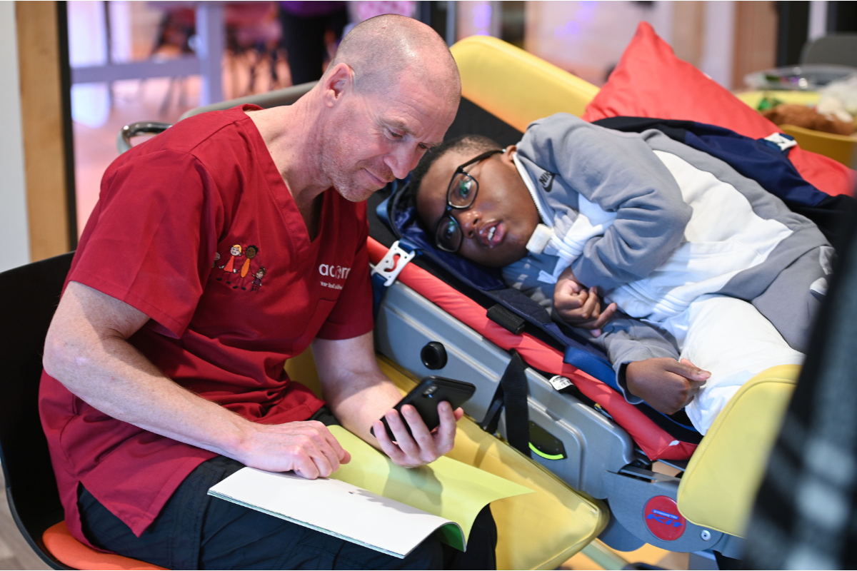 A young boy lying down and a male nurse sitting next to him.