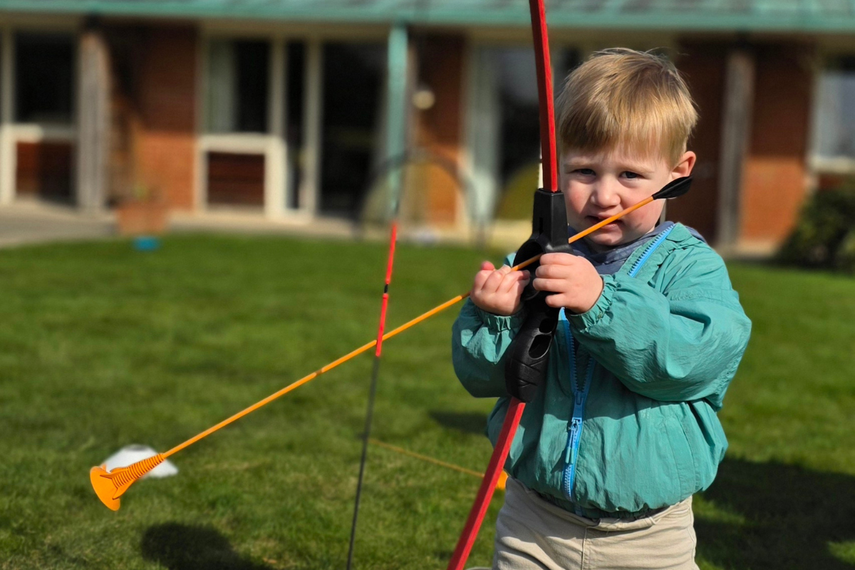 A young boy holding a large plastic bow and arrow.