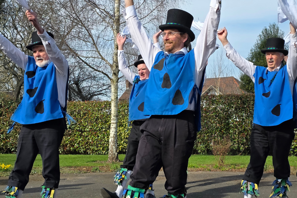 Four men wearing blue tops and top hats with their arms in the air above them.
