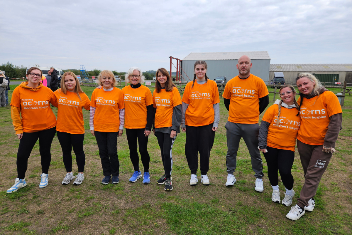 Acorns skydive A group of nine adults all wearing orange Acorns tops stood outside.