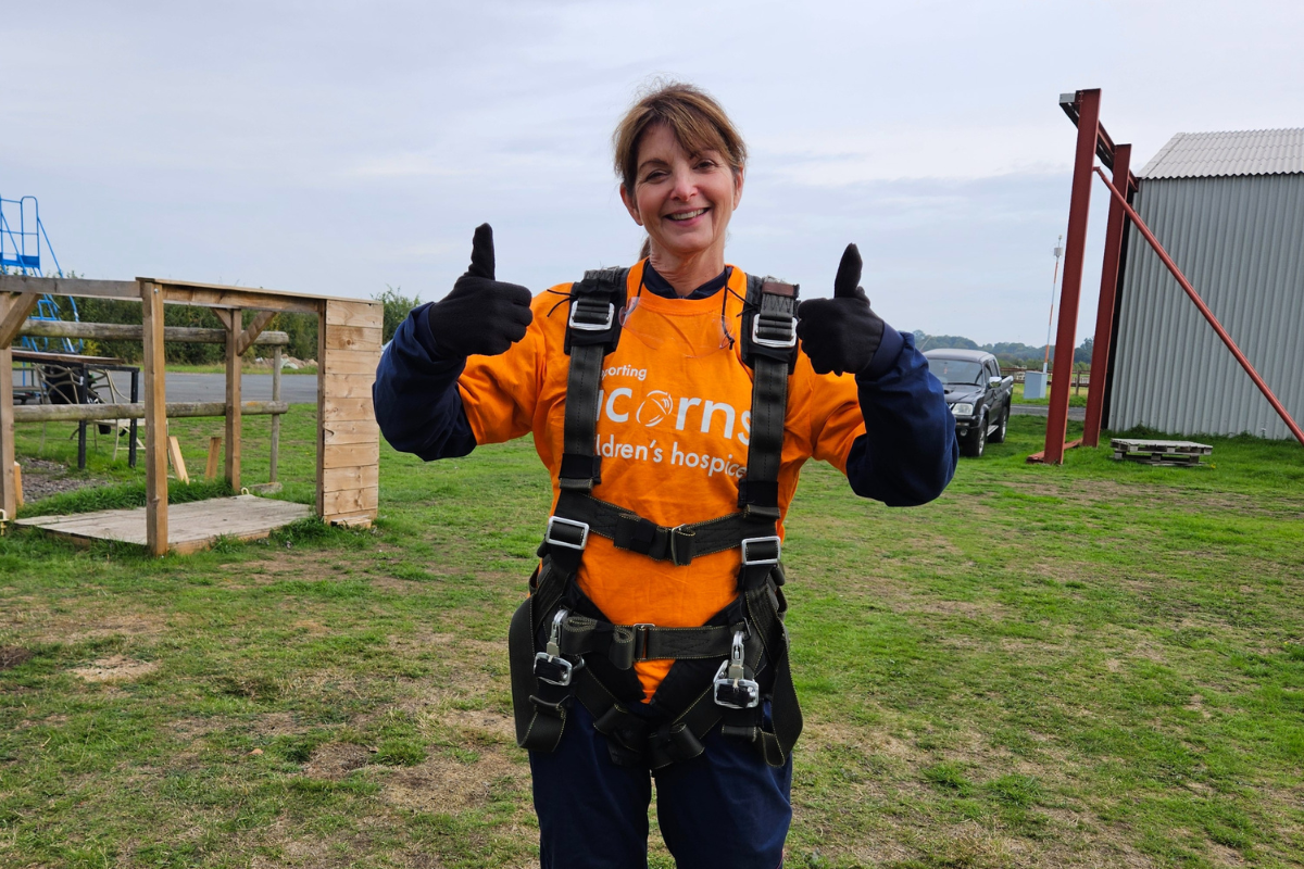 Acorns skydive A woman wearing an Acorns top and a harness smiling with her thumbs up.