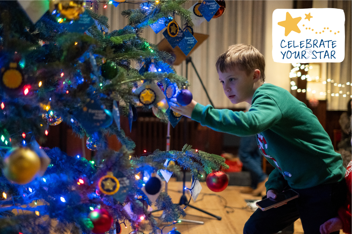 A boy looks at a star bauble on a Christmas tree at an Acorns Celebrate Your Star event