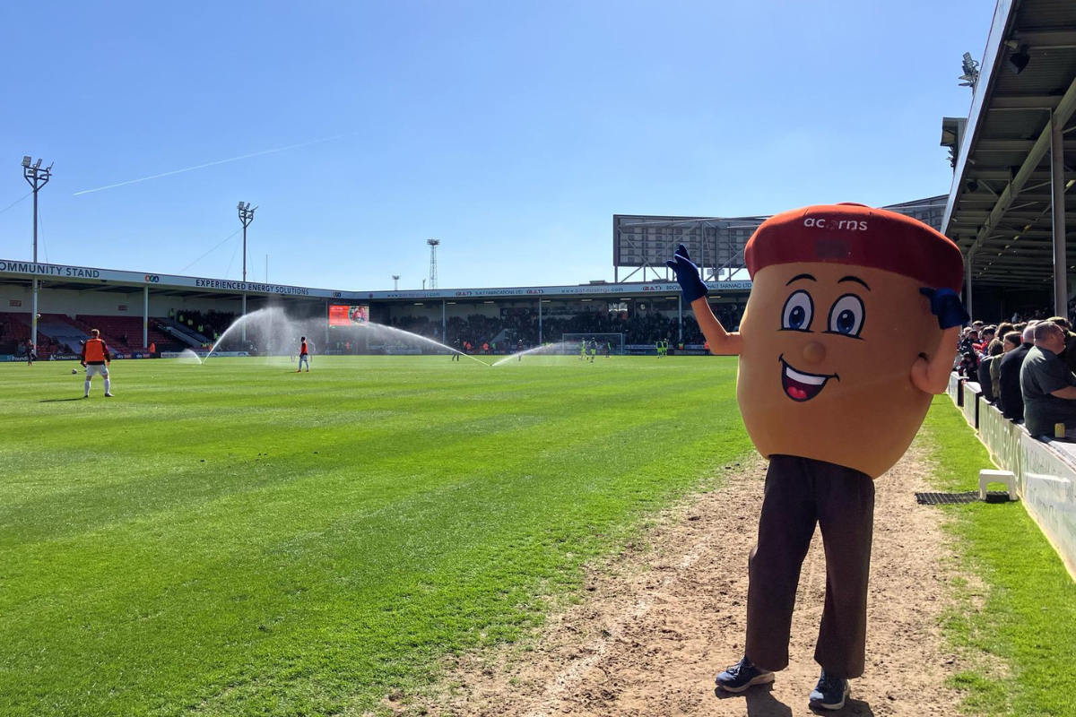 Alex the Acorn stood on the pitch grass at Bescot stadium.