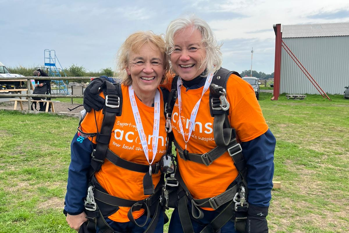 Acorns skydive Two women wearing Acorns tops and skydive harnesses with medals.