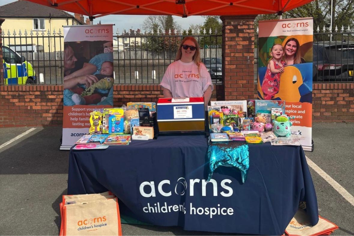 A woman stood behind an Acorns stand which is filled with toys and prizes.