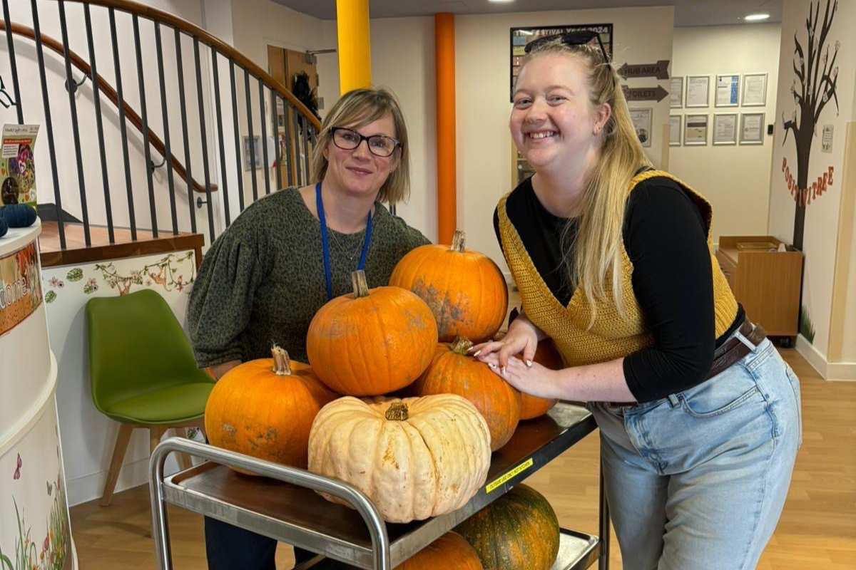 Two women smiling next to a trolley full of pumpkins.