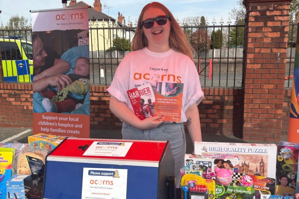 A girl wearing an Acorns t shirt behind a stand full of toys and prizes.