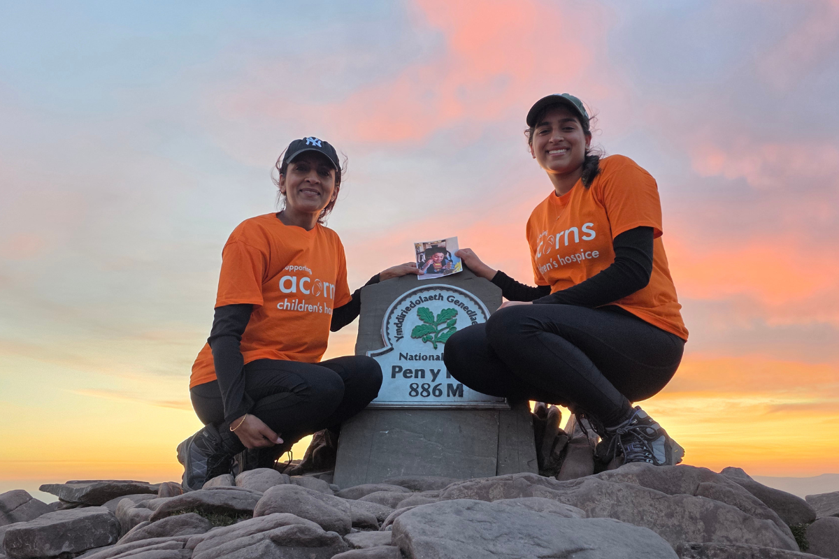Two women wearing orange Acorns tops stood at the peak of Pen y Fan.