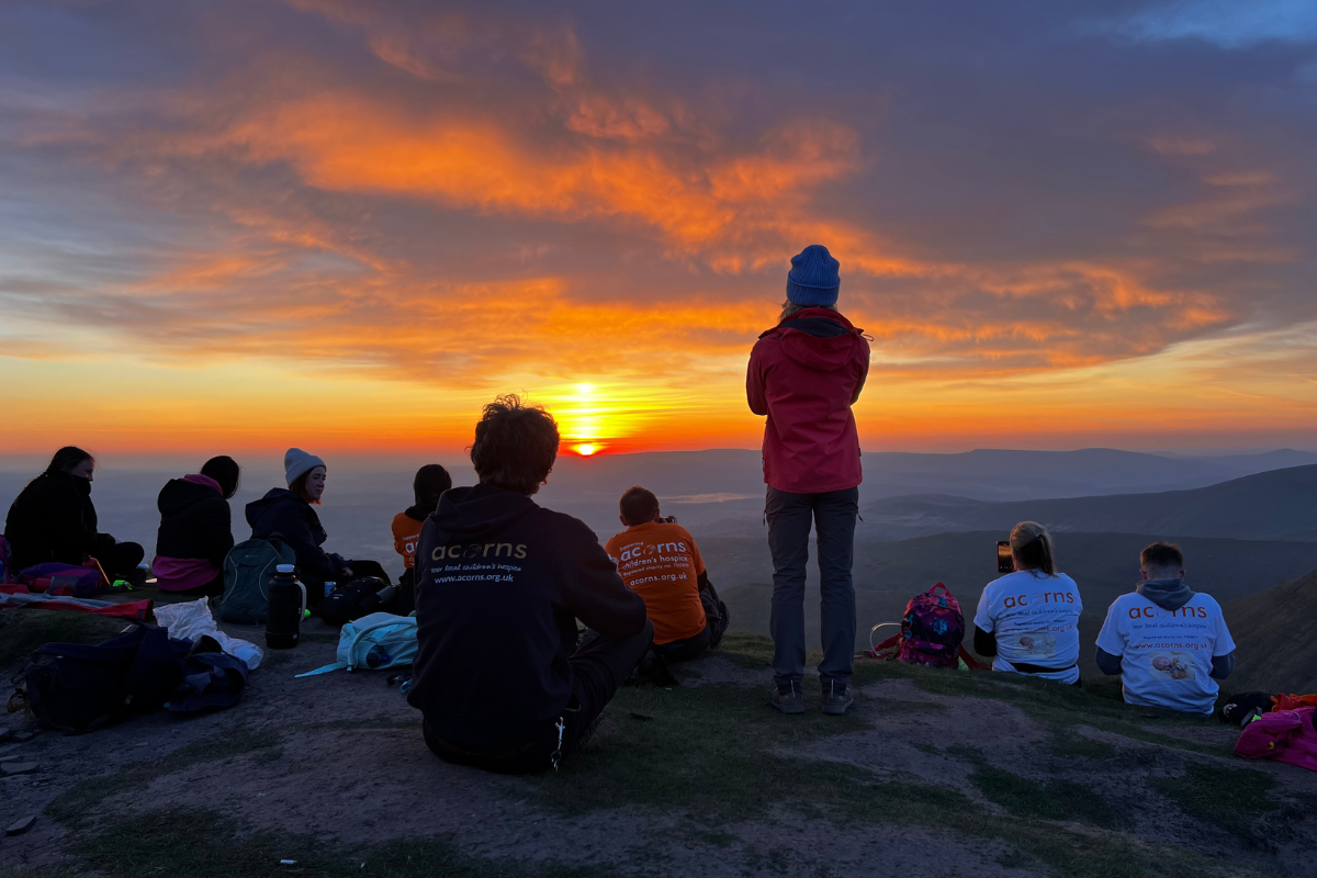 A group of people all watching the sun rising on top of Pen y Fan.