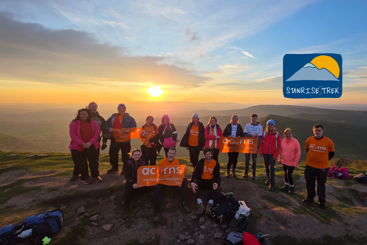 A large group of people wearing orange Acorns tops stood on top of Pen y Fan at sunrise.