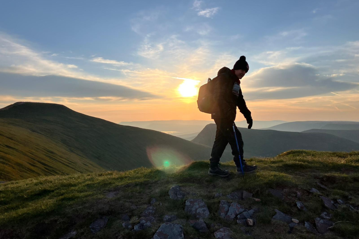 A man walking on a hill as the sun rises.