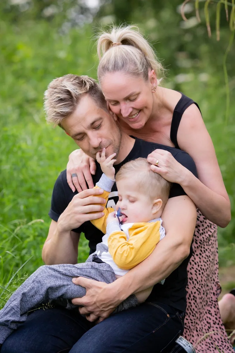 A man and woman looking down at a young boy in the man's arms. The boy is touching the man's face