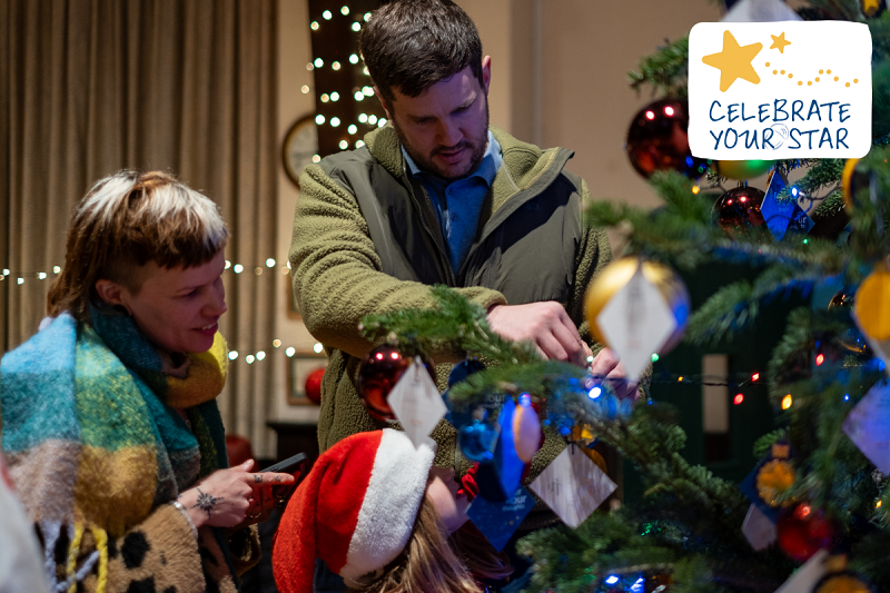 Two people looking at a dedication on a Christmas tree at an Acorns Celebrate Your Star event