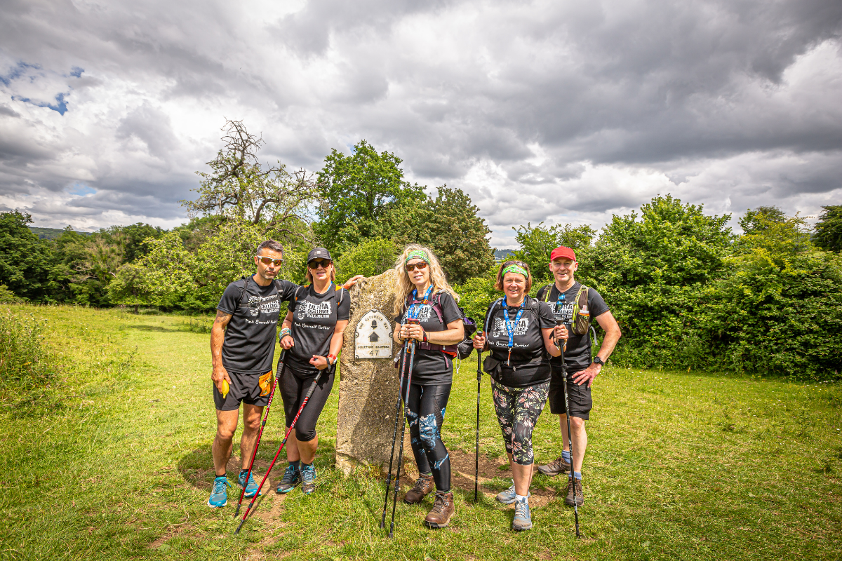 Five people holding hiking sticks stood next to a rock with a sign on it.