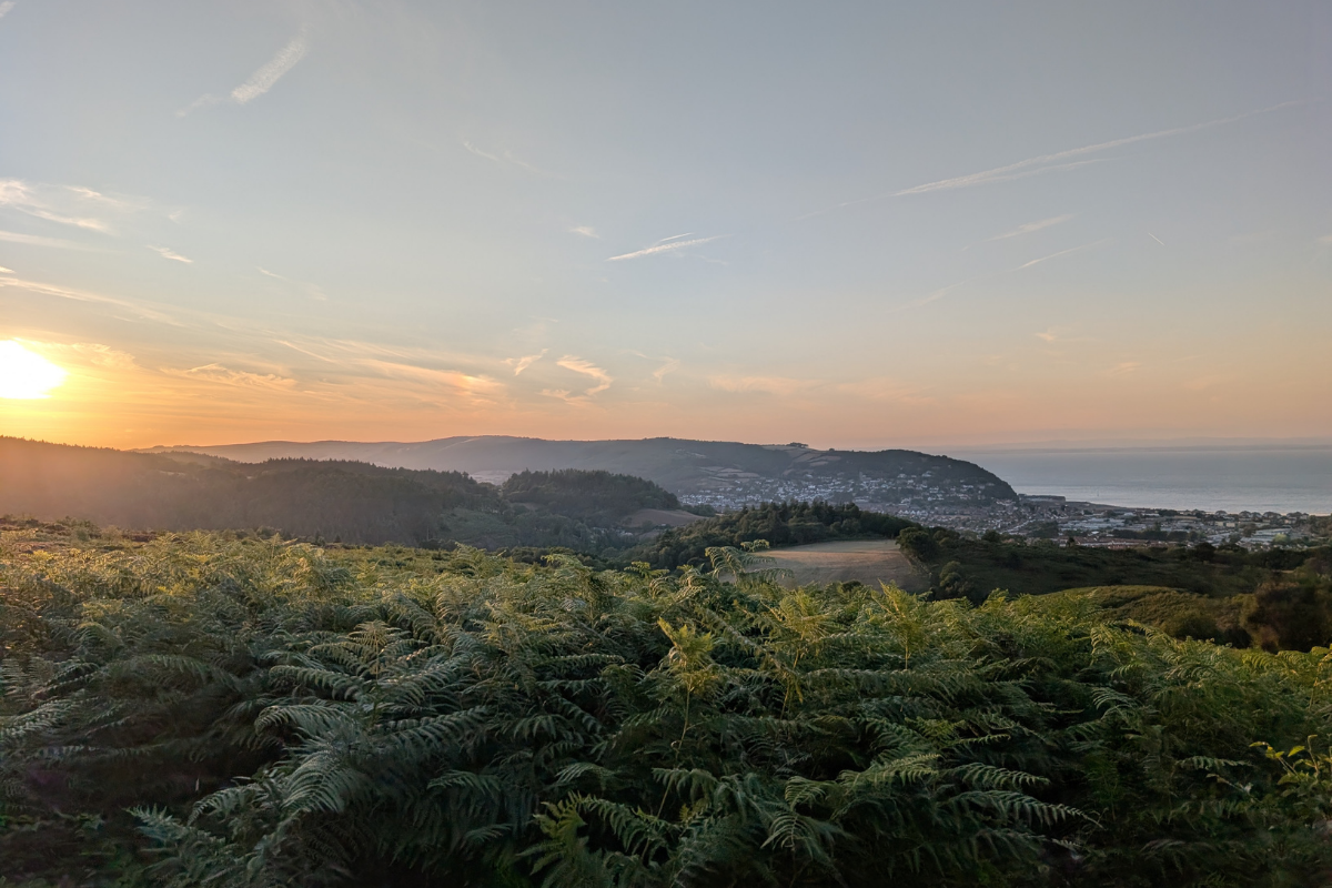A sunset over grassy hills and coastal cliffs.