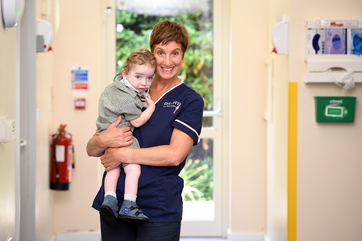 A member of Acorns Care team holds a small child who has a breathing tube