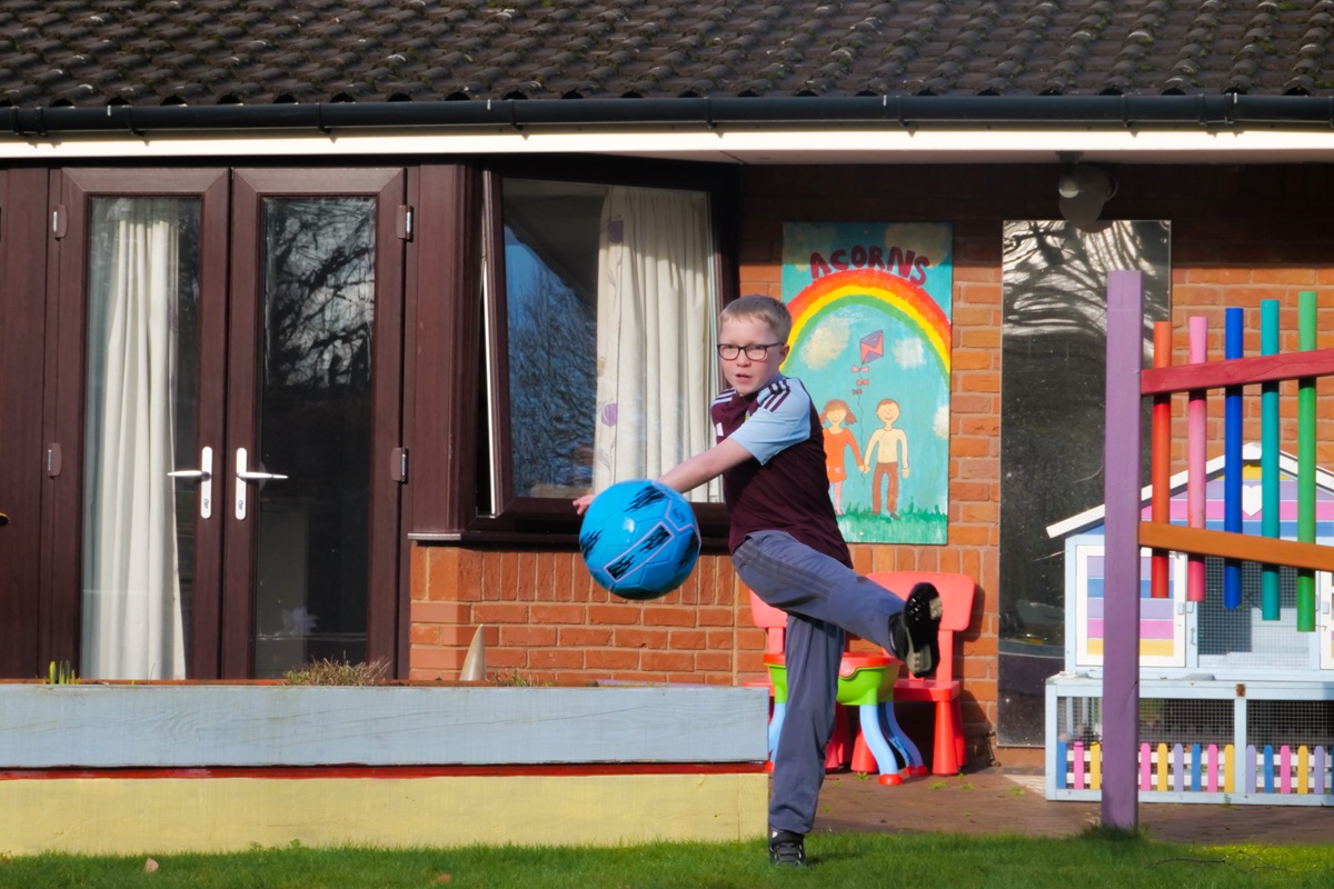 A boy in an Aston Villa top kicks a football in an Acorns hospice garden