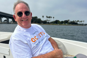 John Scott wearing sunglasses and a white Acorns top on a boat in the sea.