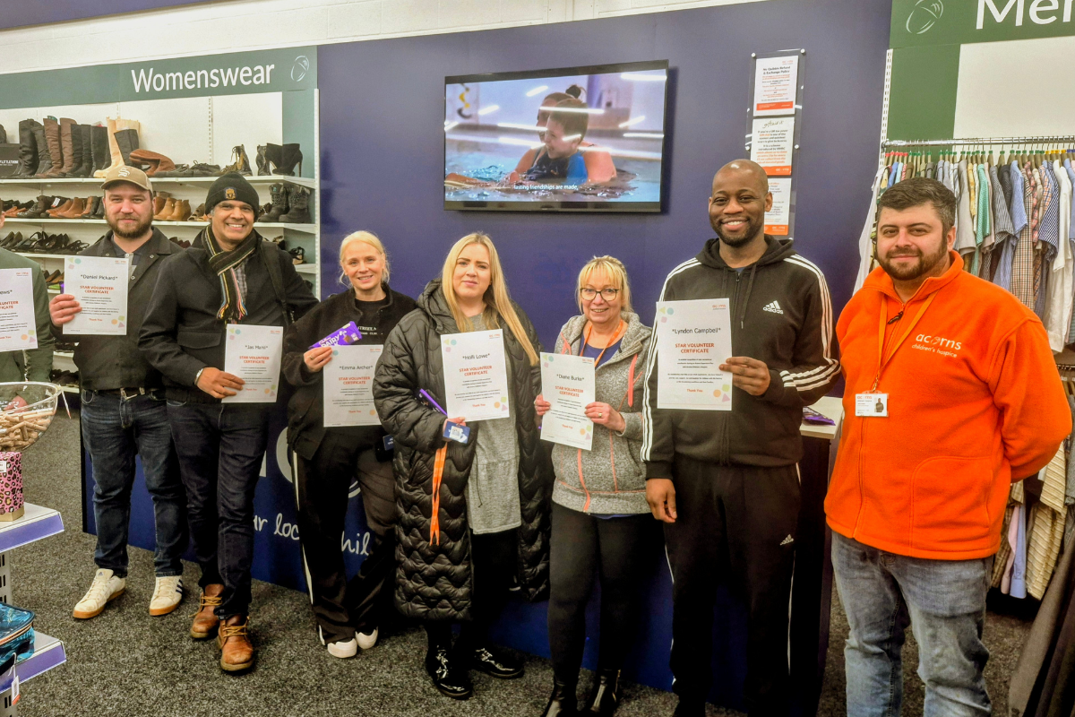 Seven people stood side-by-side in a shop, each holding up an A4 star volunteer certificate.
