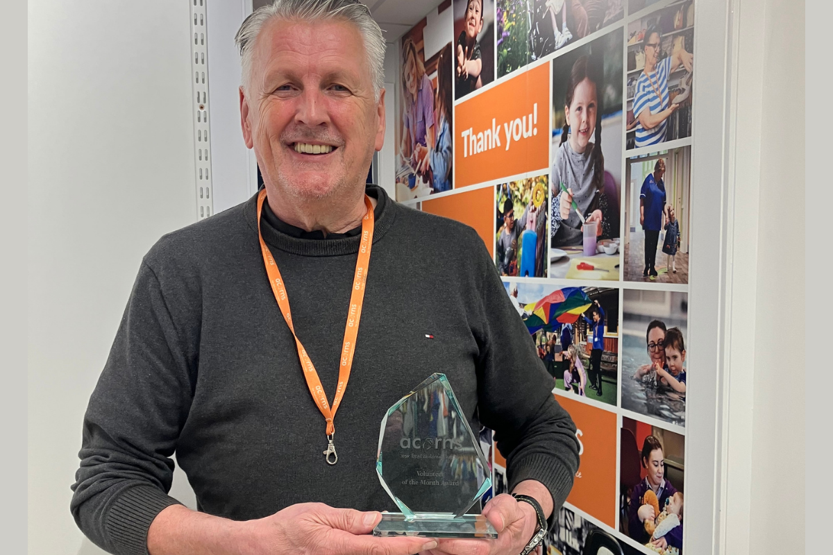A man wearing an orange lanyard and smiling. He is holding a small award in his hands.