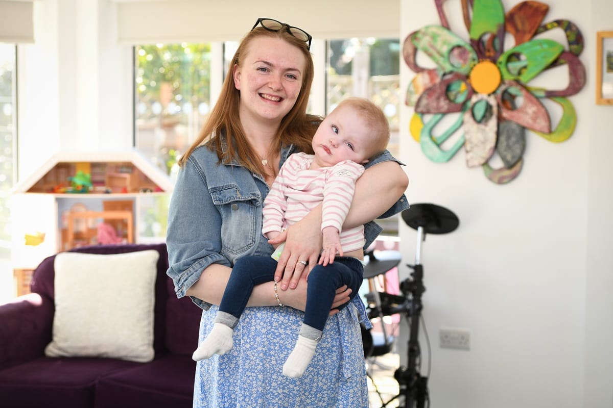 A smiling woman stands in an Acorns hospice with a young child in her arms