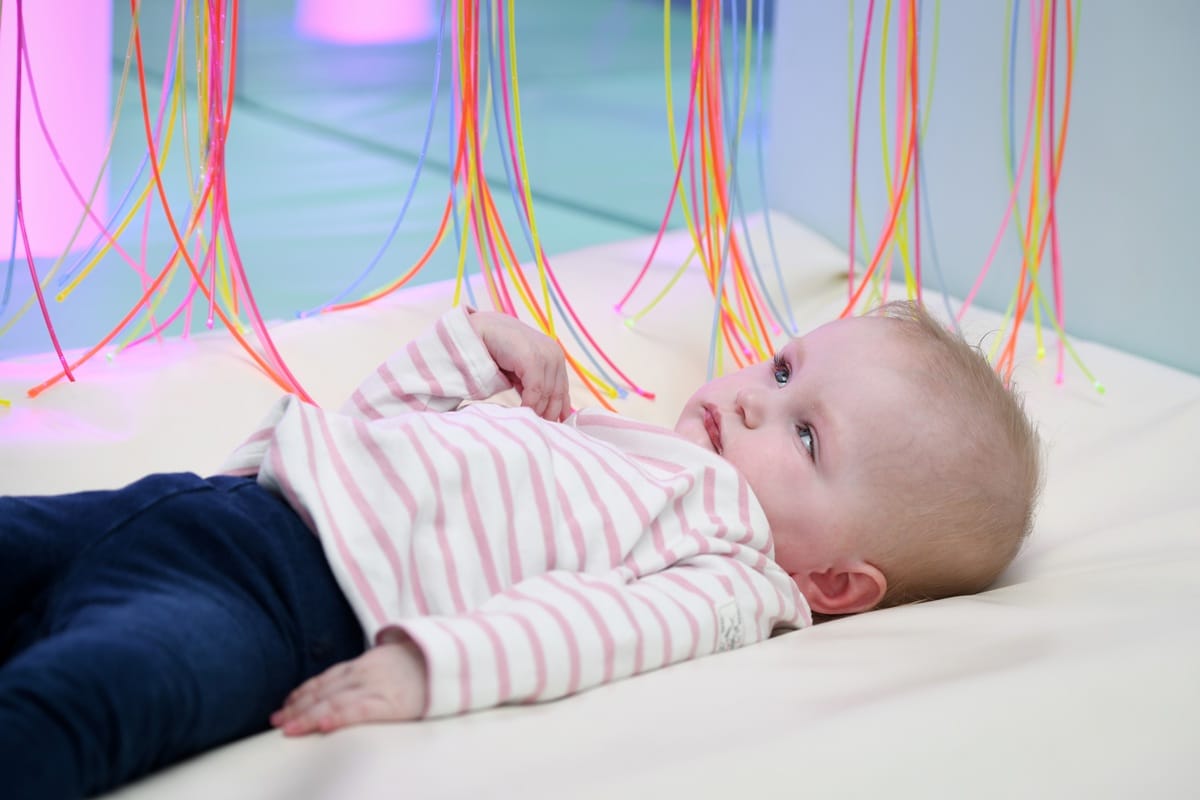 A young child lays in an Acorns sensory room looking at multicoloured strands of lights