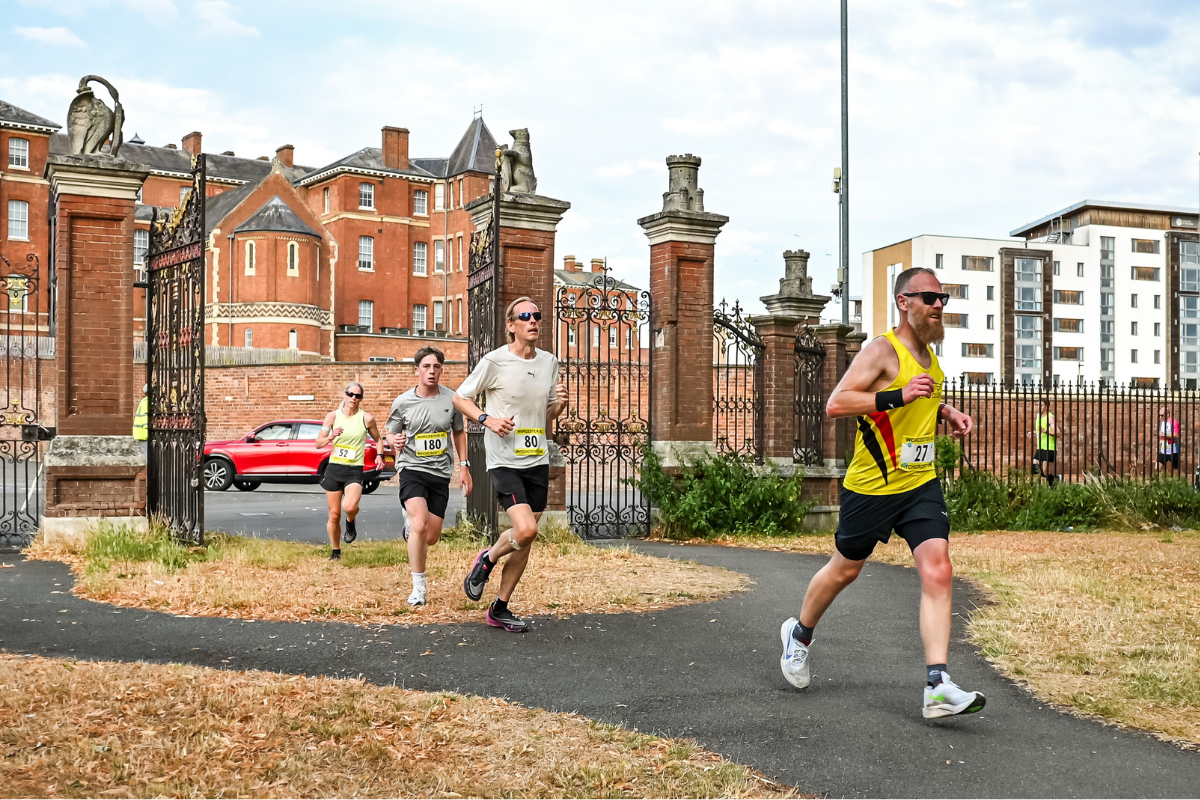 Runners racing through a gate into a park in the Worcester Pitchcroft 10k