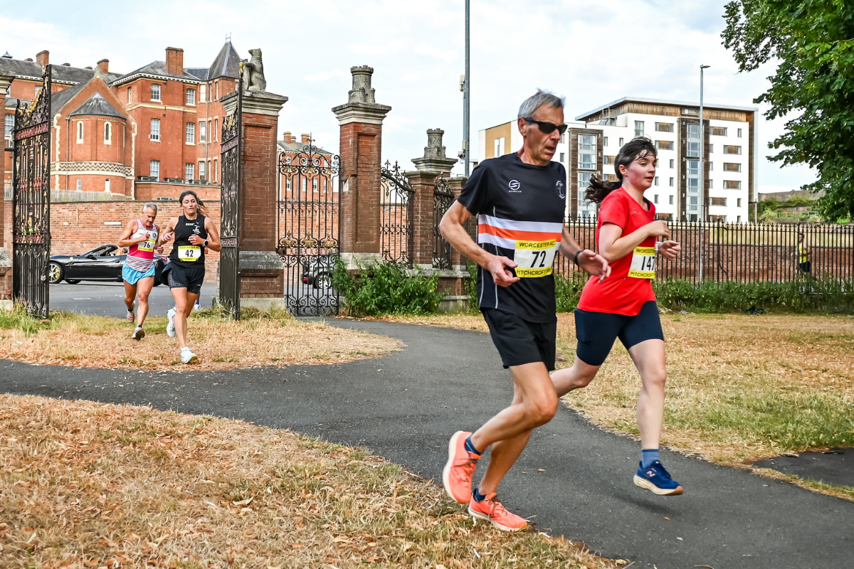 Runners racing through a gate into a park in the Worcester Pitchcroft 10k