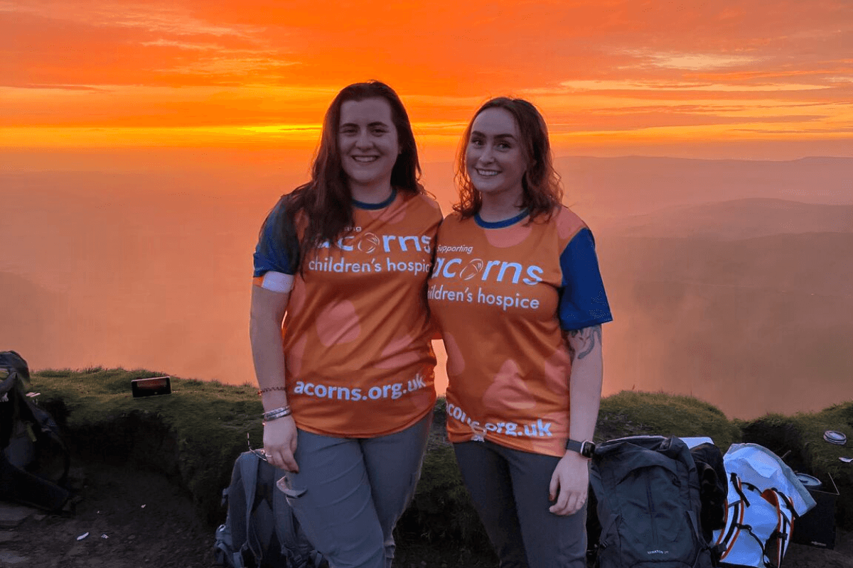 Kit size Two women wearing orange Acorns t shirts with a bright orange sunset behind them.