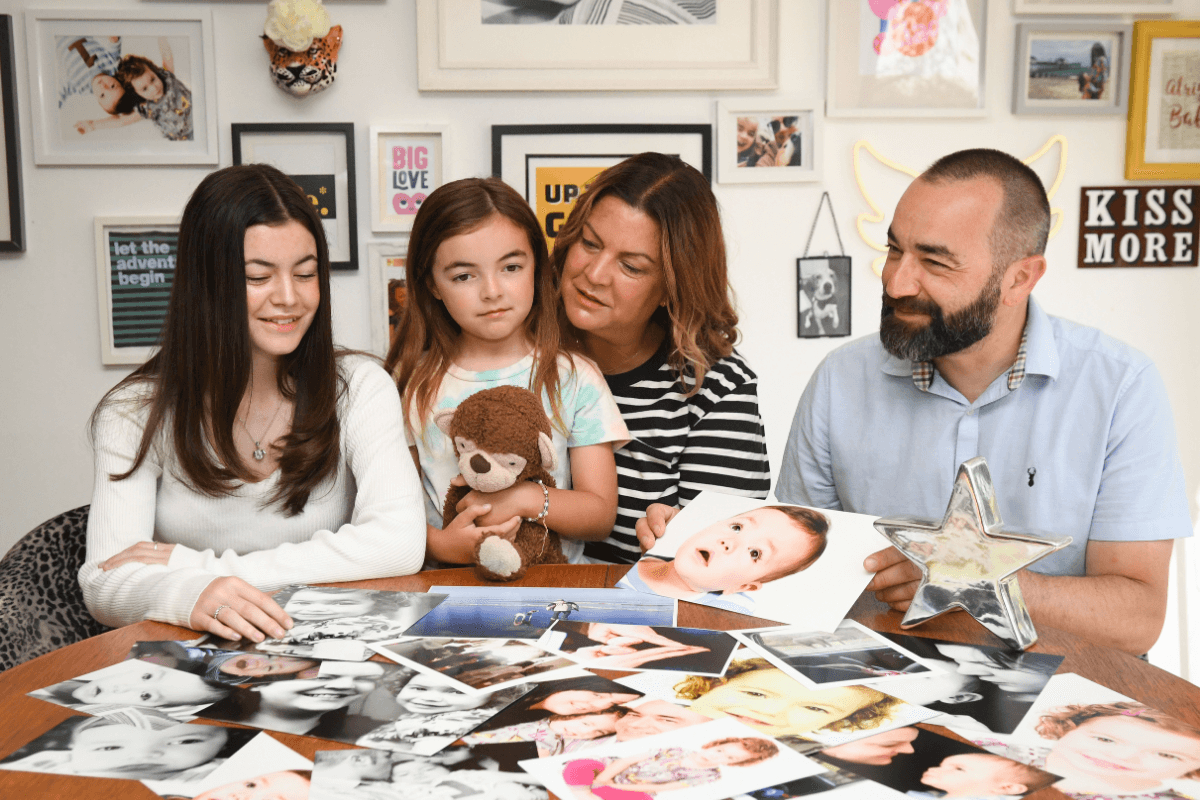 A family with two daughters and their parents sat around table looking at lots of photos of their son.