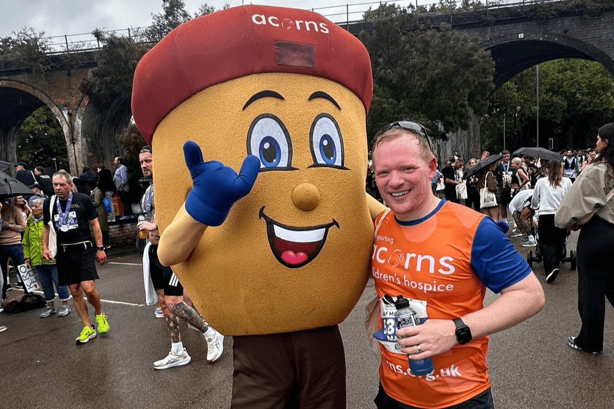 WCR 27 A man wearing an Acorns running vest taking a photo with an Acorn mascot.