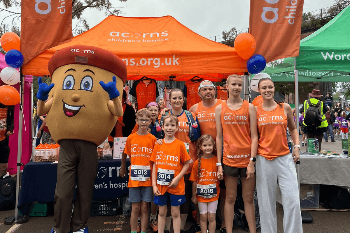 WCR 27 A group of eight people, mostly children all wearing Acorns running vests, stood next to an Acorn mascot.