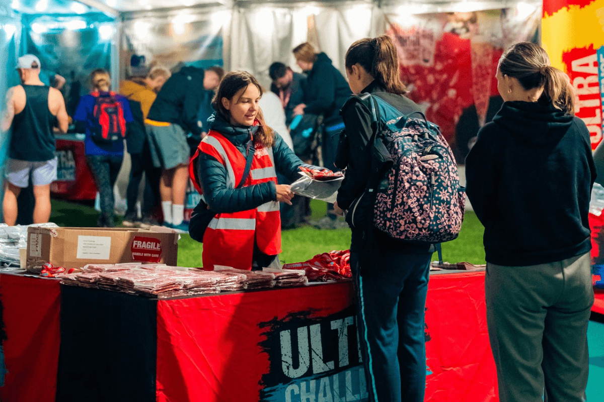 Kent Downs 50 A woman wearing a red hi vis jacket at an Ultra Challenge stand, speaking to two women.